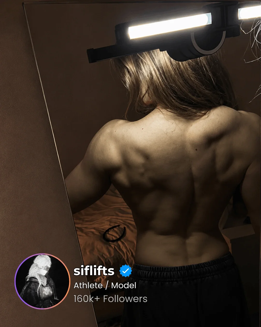 Athlete's back in a mirror lit by a GYMLIGHT bar clamped to the top of the mirror