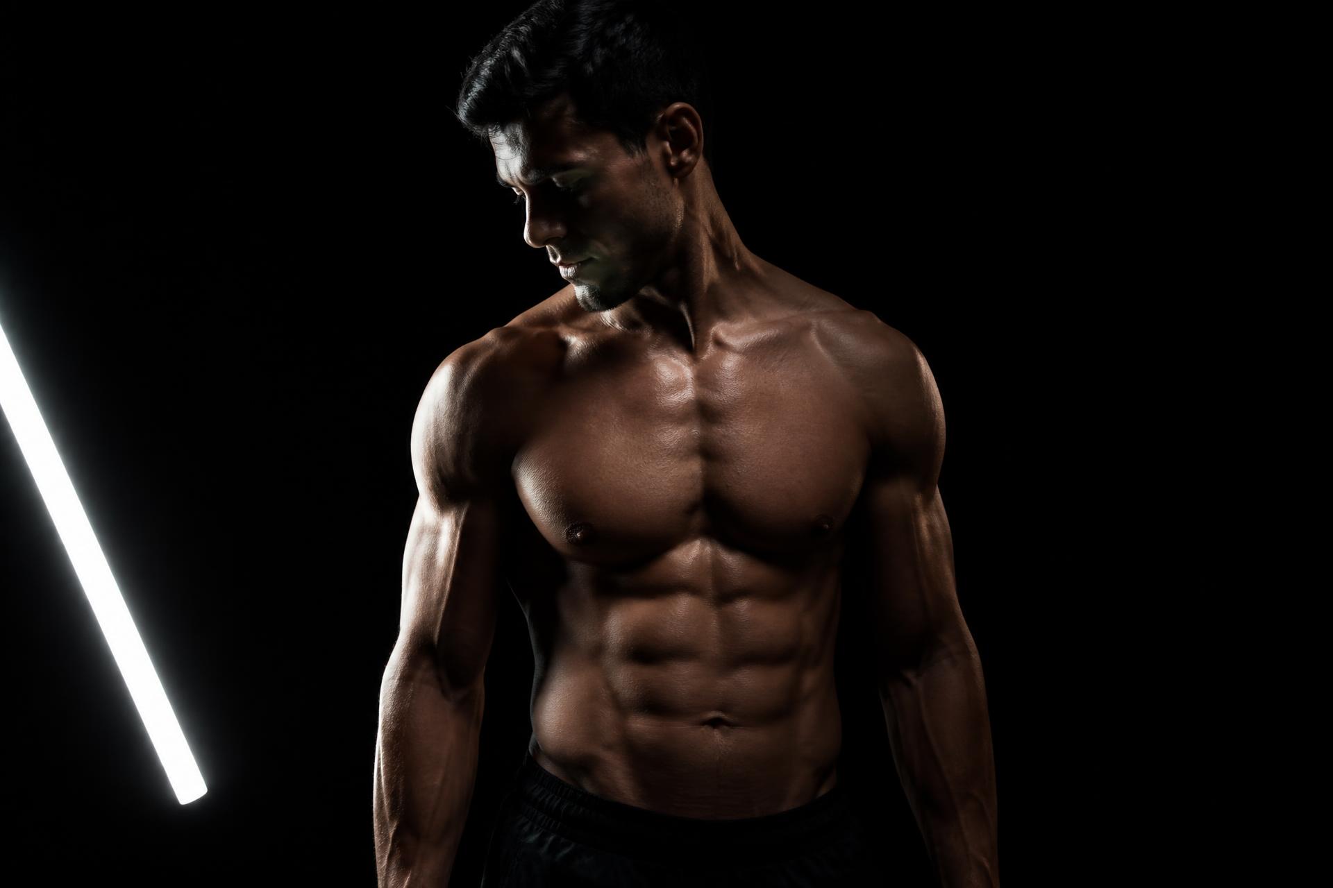 Athlete in a dark gym lit from the front by a GYMLIGHT light bar, muscle definition sharply modelled
